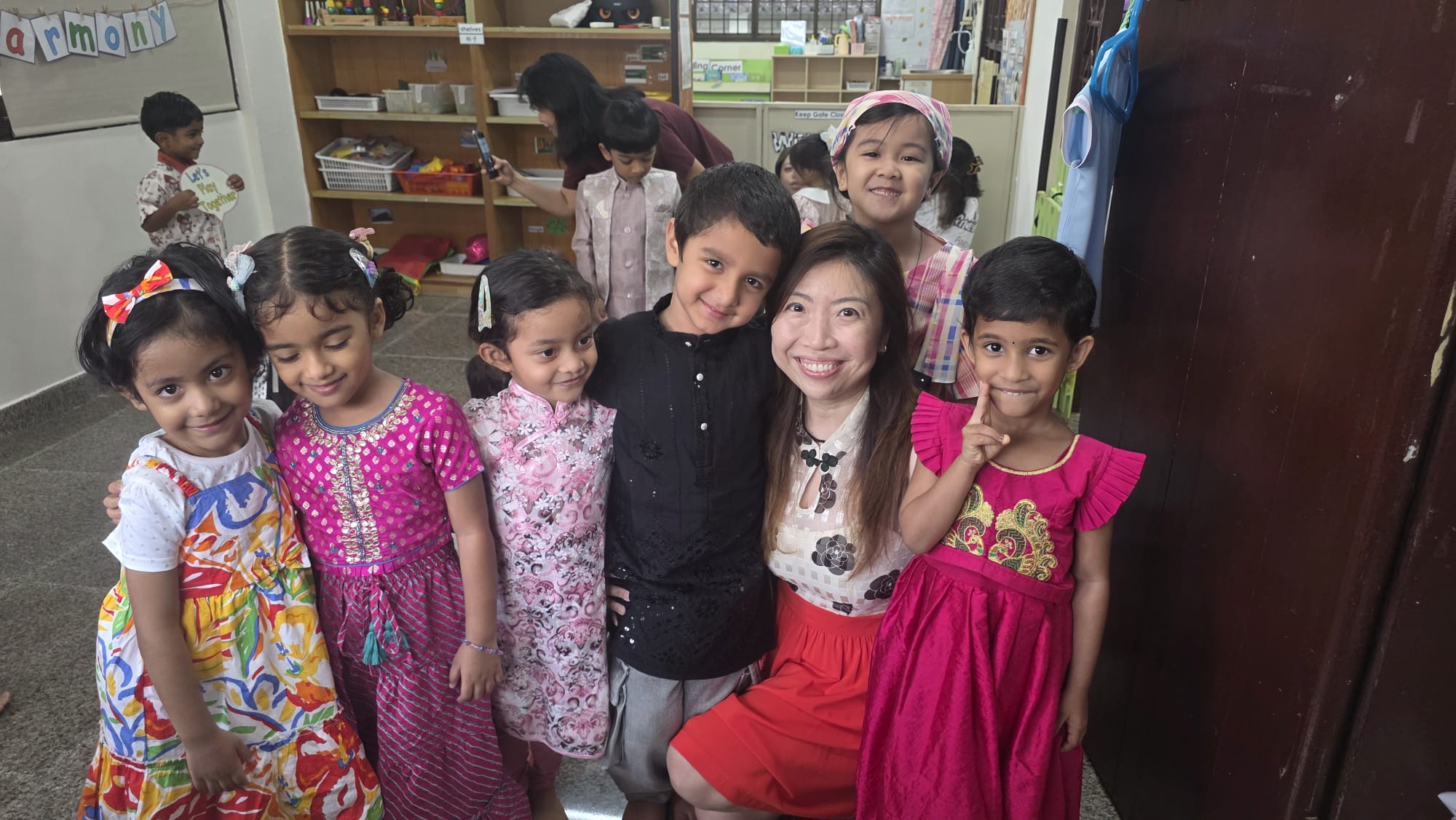 The founder of Genius Gems with a group of smiling children in traditional dress at the Changi centre
