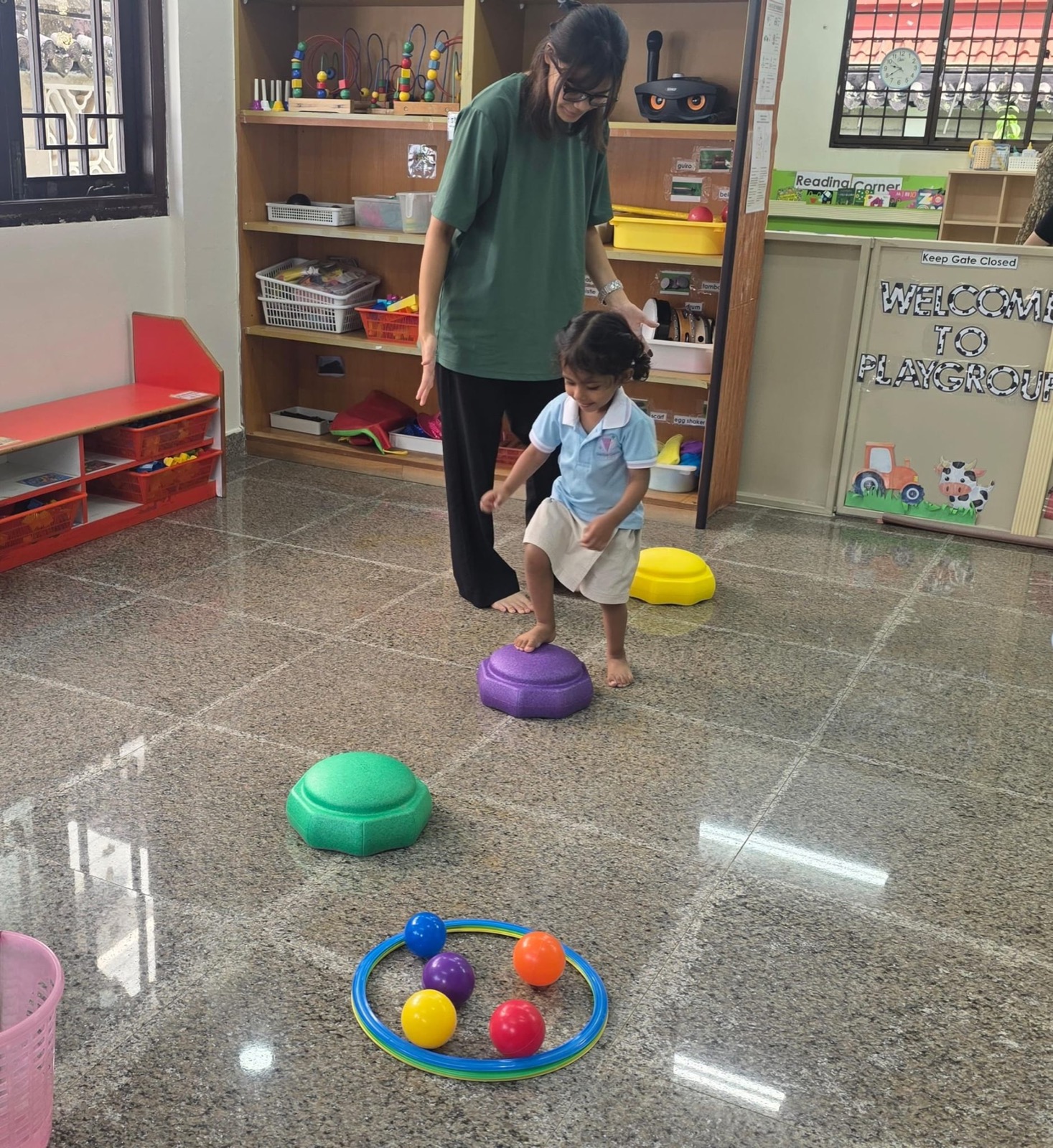 A Genius Gems teacher guiding a toddler across colourful stepping stones during a playgroup balance activity