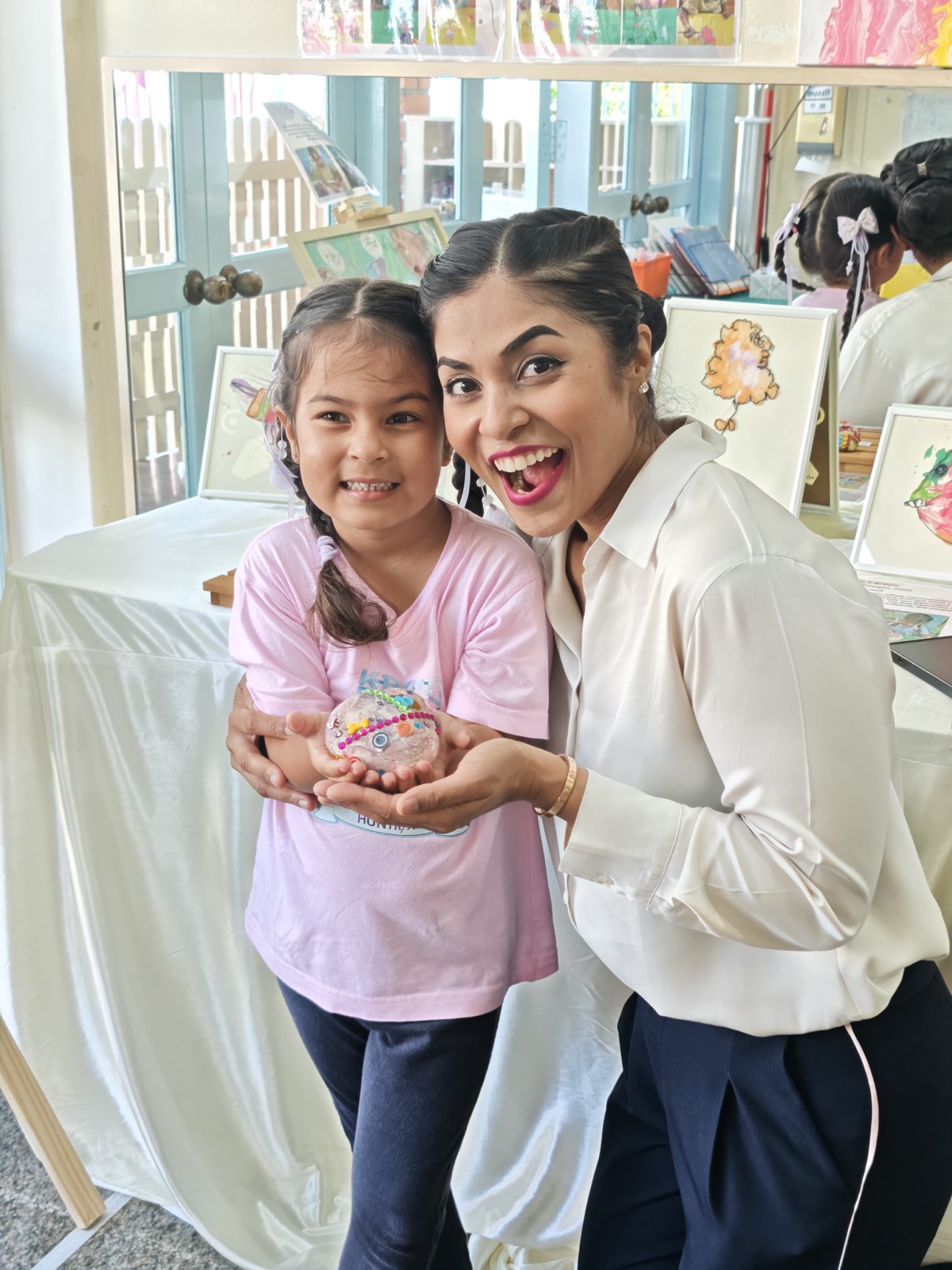 A parent and child beaming together while holding the child's decorated artwork at a Genius Gems family showcase